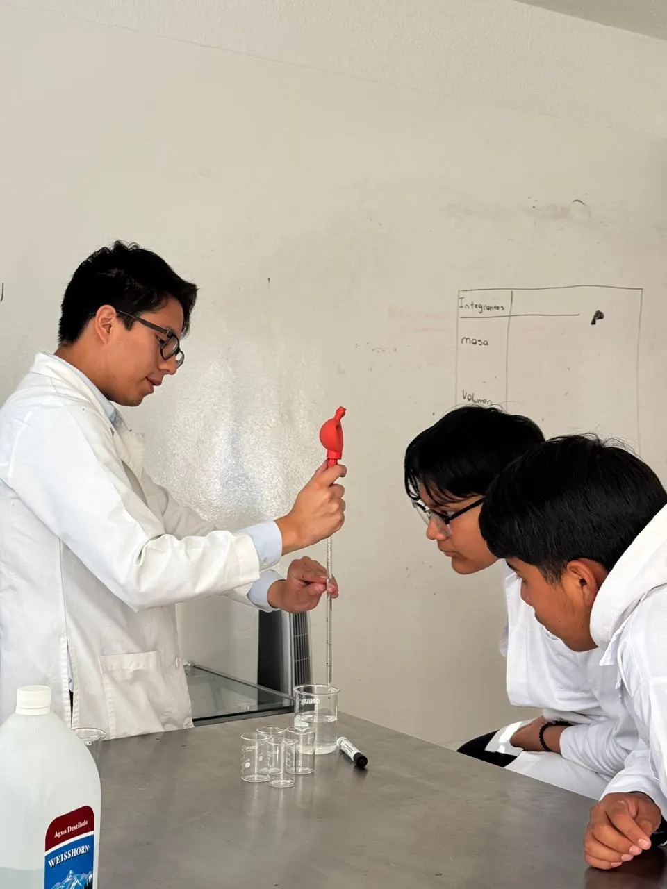 Alumnos con bata realizando una práctica en el laboratorio de química